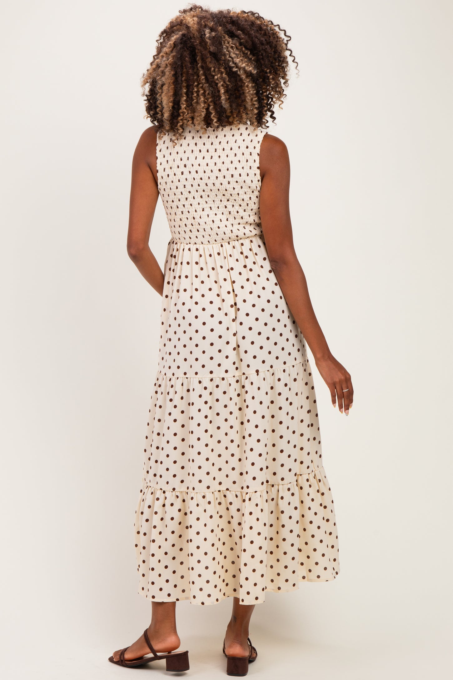 woman wearing a beige maternity dress with black polka dots and a tiered hem, showing the back view