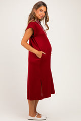 woman wearing a burgundy maternity dress with short sleeves and side pockets, showing her baby bump