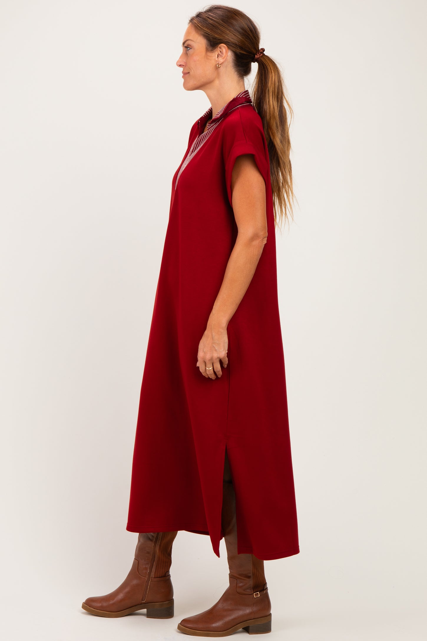 woman wearing a burgundy oversized dress with short sleeves and side slits, paired with brown knee-high boots