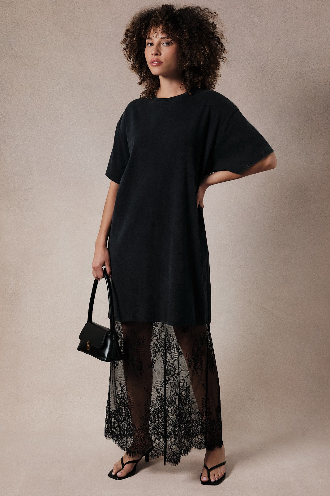 woman wearing a black oversized t-shirt dress layered with a black lace maxi skirt and holding a small handbag
