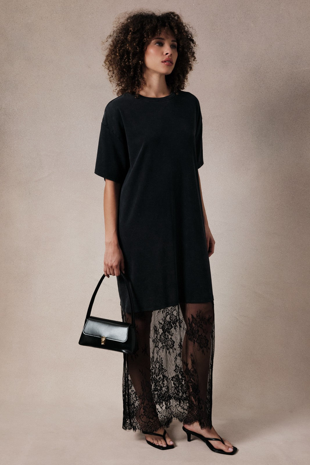 woman wearing a black oversized t-shirt dress with a lace overlay and carrying a black handbag