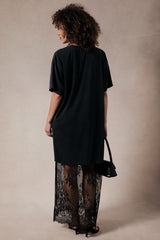 woman wearing a black oversized t-shirt dress with a sheer lace hem and holding a small black bag