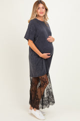 woman wearing a dark gray maternity dress with a lace overlay and holding her baby bump