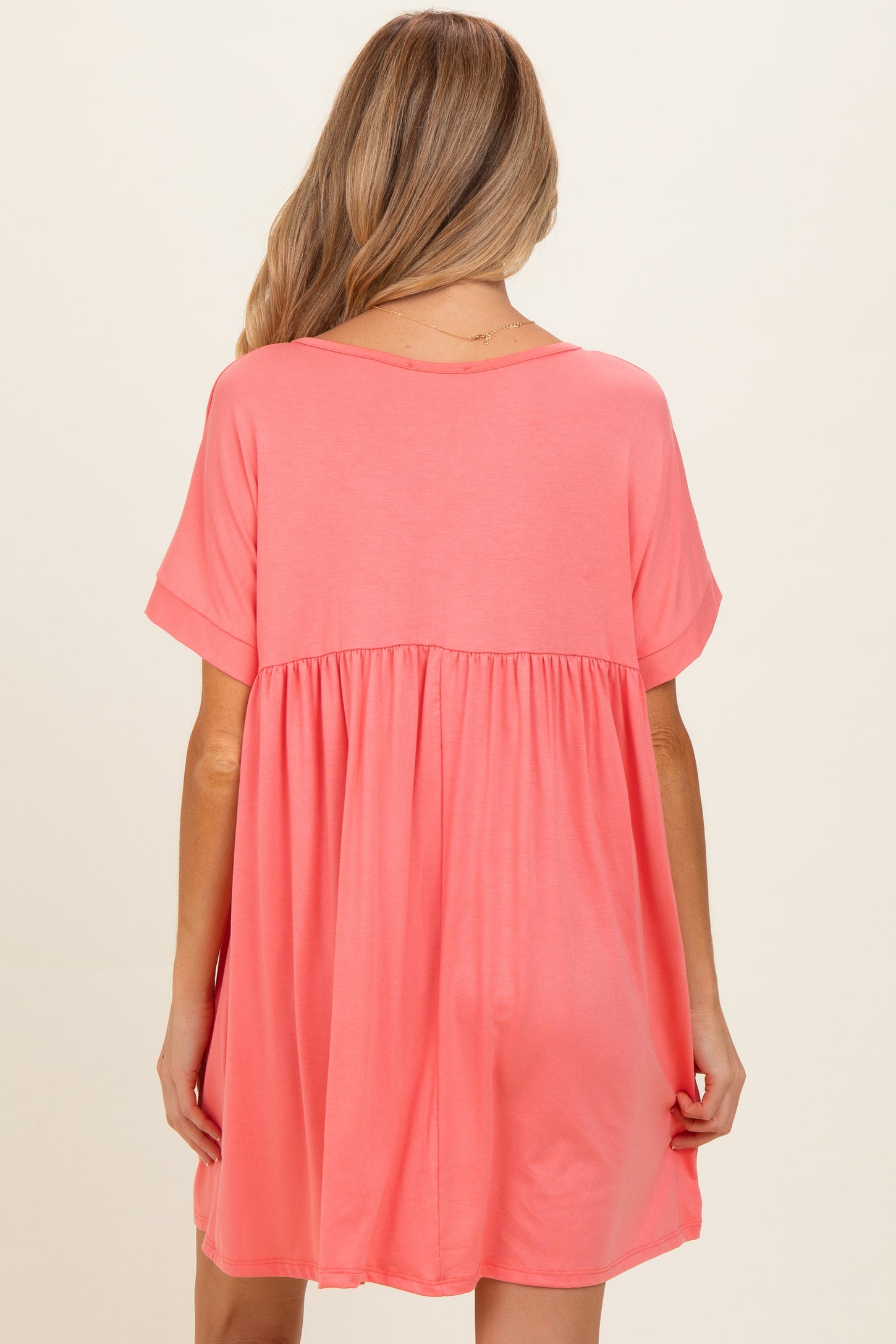 woman wearing a coral pink maternity dress with a relaxed fit and short sleeves, showing a flowing style from the waist down