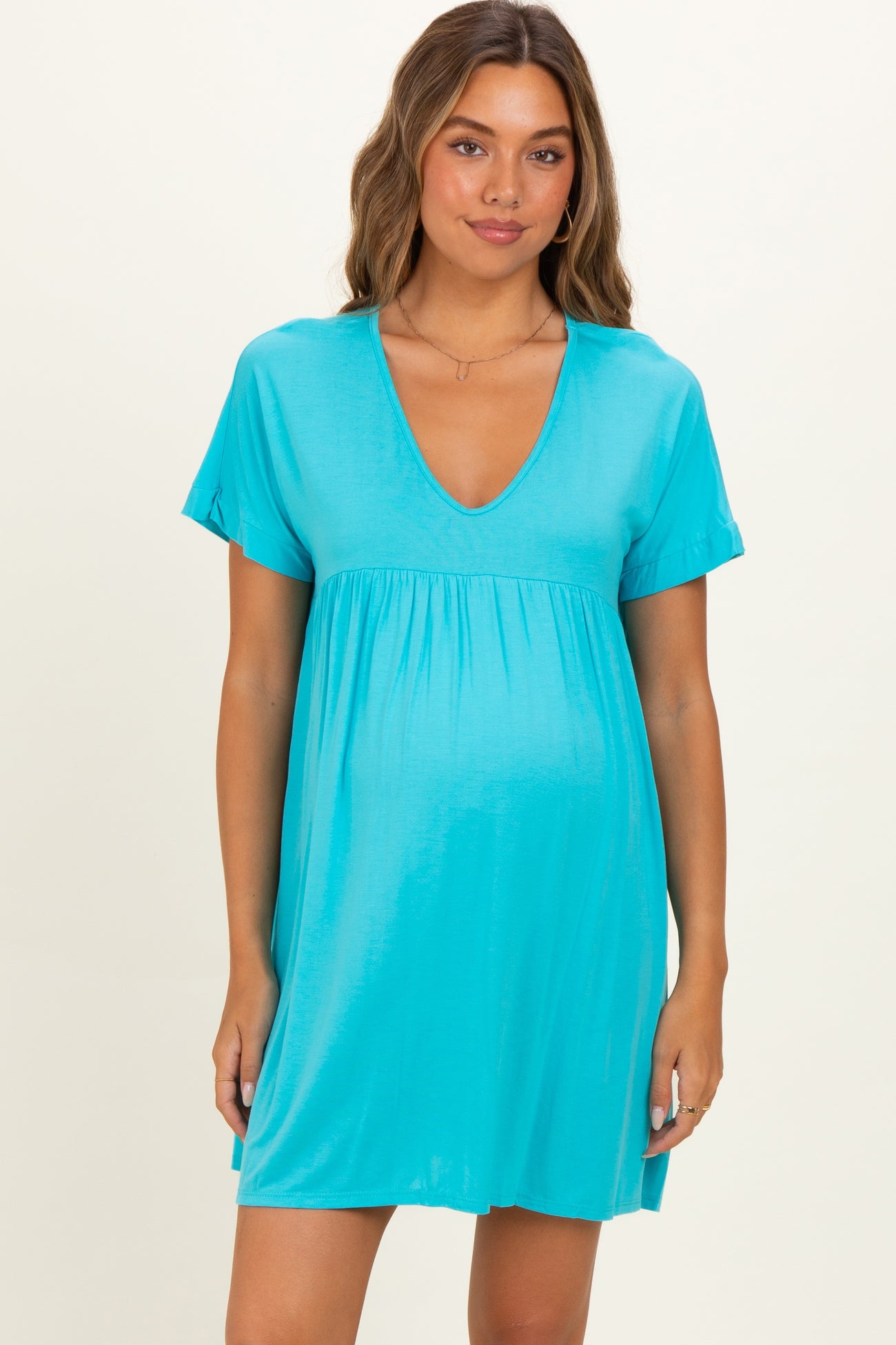 woman wearing a turquoise maternity dress with short sleeves and a v-neck, showing her baby bump