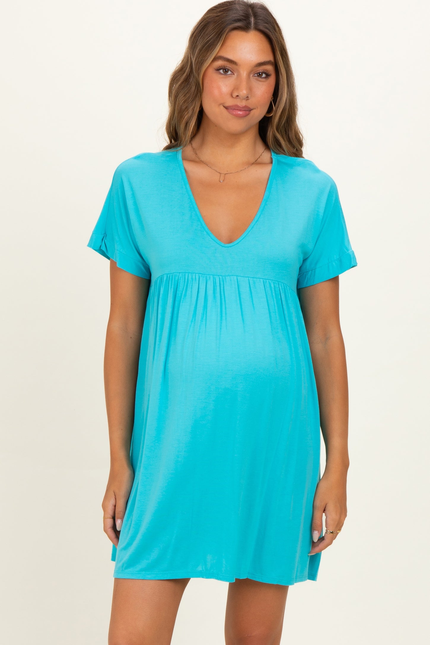 woman wearing a turquoise maternity dress with short sleeves and a v-neck, showing her baby bump