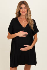 woman wearing a black maternity dress with a v-neck and short sleeves, holding her baby bump