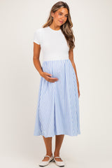 woman wearing a white short sleeve maternity dress with a light blue and white striped skirt, holding her baby bump