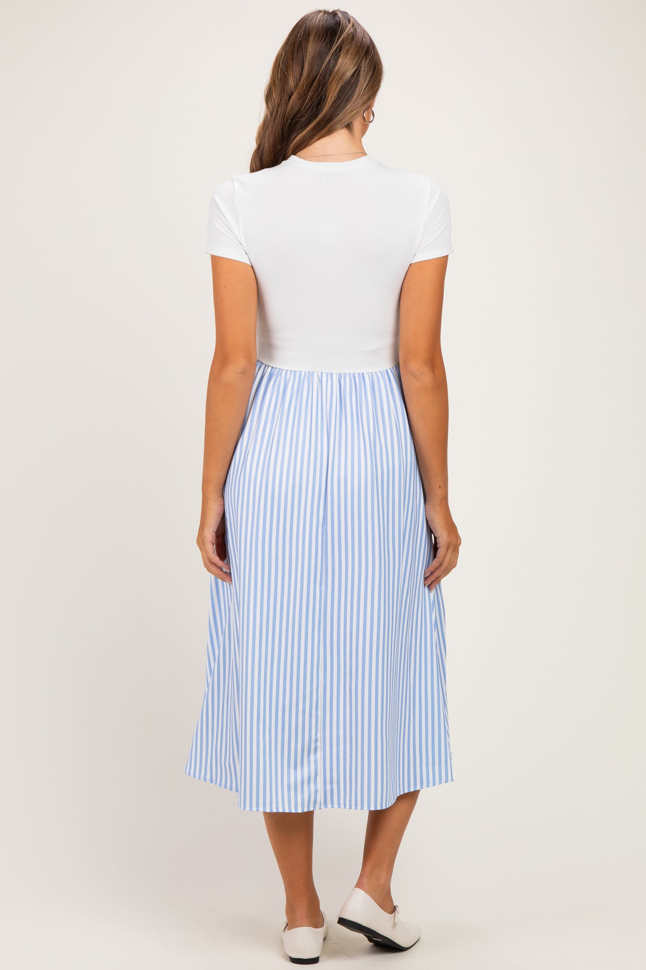 woman wearing a white and light blue striped maternity dress with a fitted top and flowy skirt, showing her baby bump