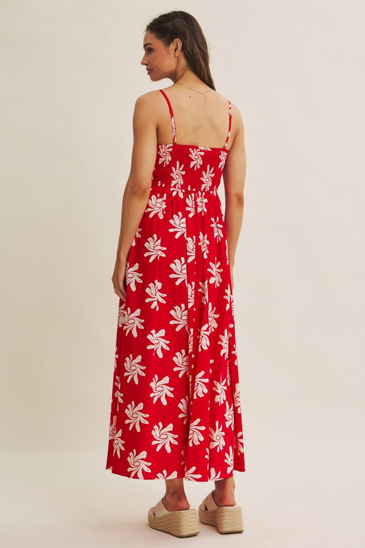 woman wearing a red floral maxi dress with spaghetti straps and a tiered skirt, viewed from the back