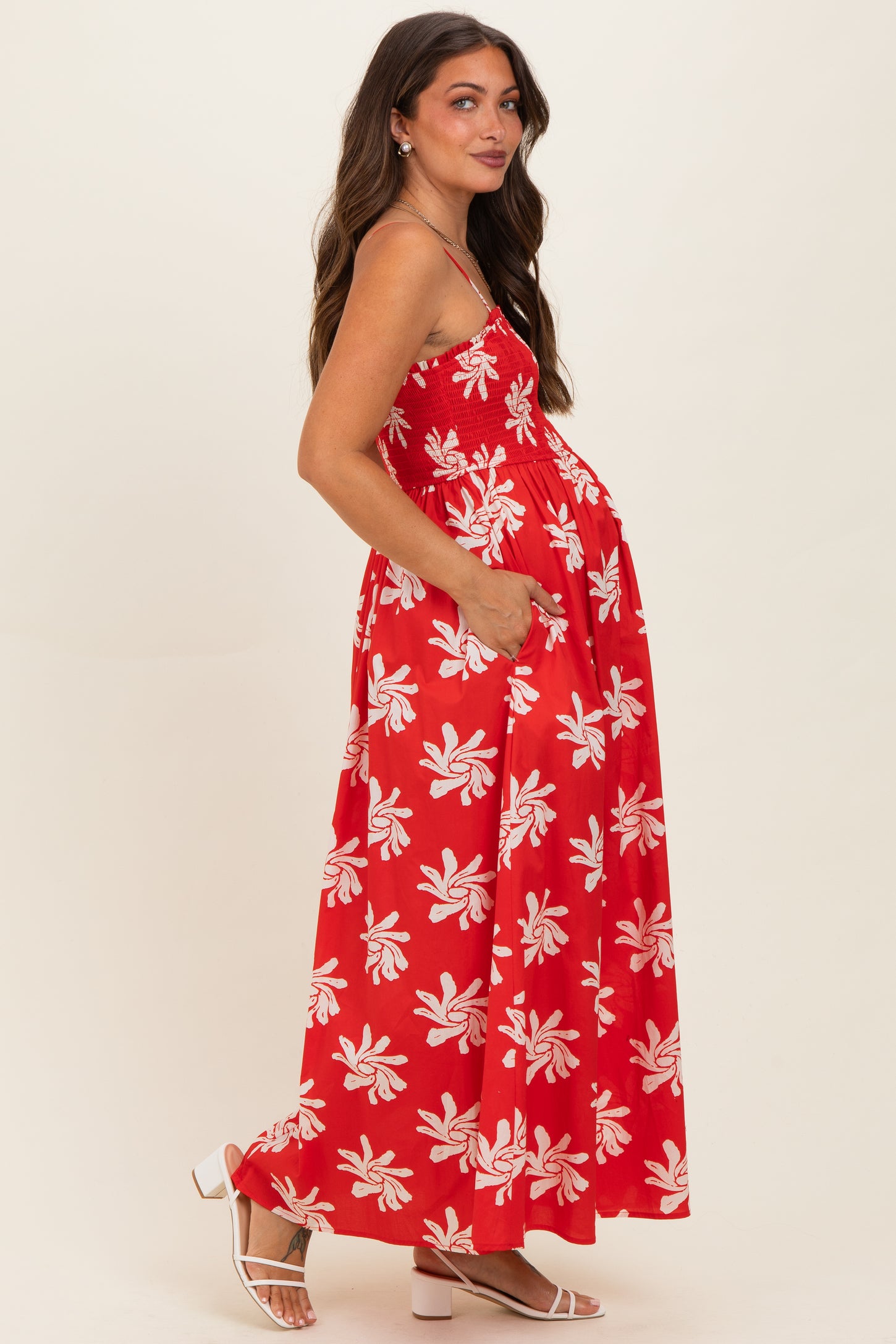 woman wearing a red maternity maxi dress with white floral patterns and adjustable straps, showing her baby bump