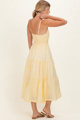 woman wearing a yellow tiered midi dress with adjustable straps, showing the back and a relaxed fit