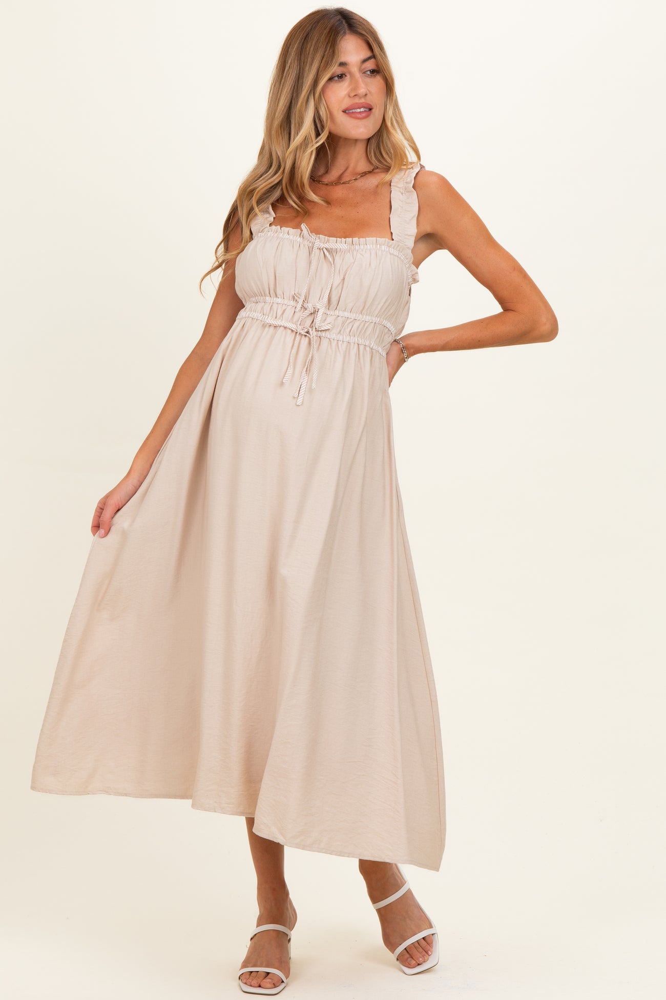 woman wearing a light beige maternity maxi dress with ruffled straps and an adjustable drawstring waist