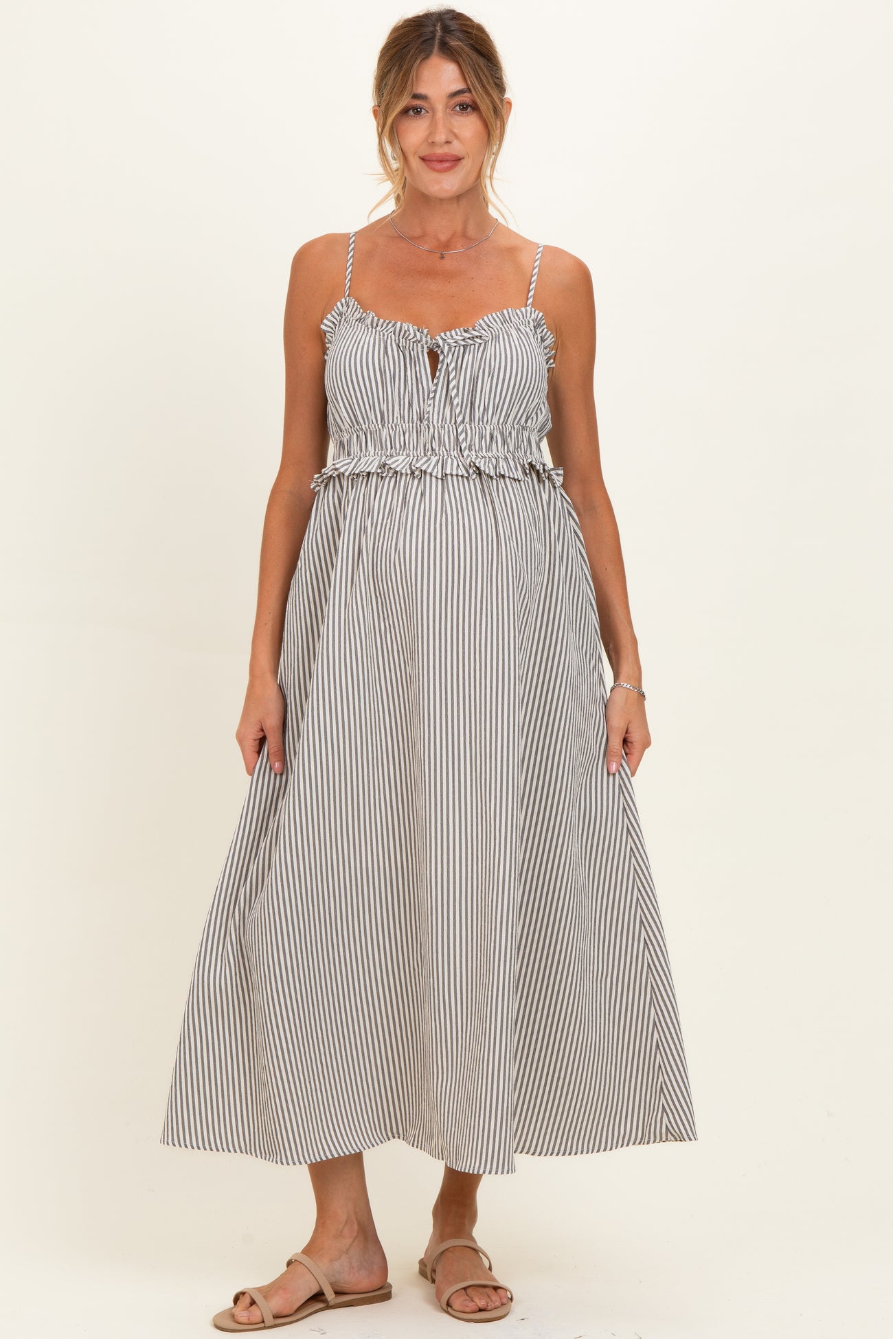 woman wearing a black and white striped maternity maxi dress with a ruffled waistband and adjustable straps