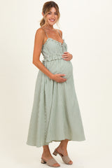 woman wearing a green and white striped maternity dress with a gathered waist and holding her baby bump