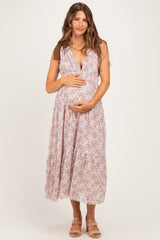 woman wearing a light pink floral maternity dress with a deep v-neck and tiered skirt, holding her baby bump