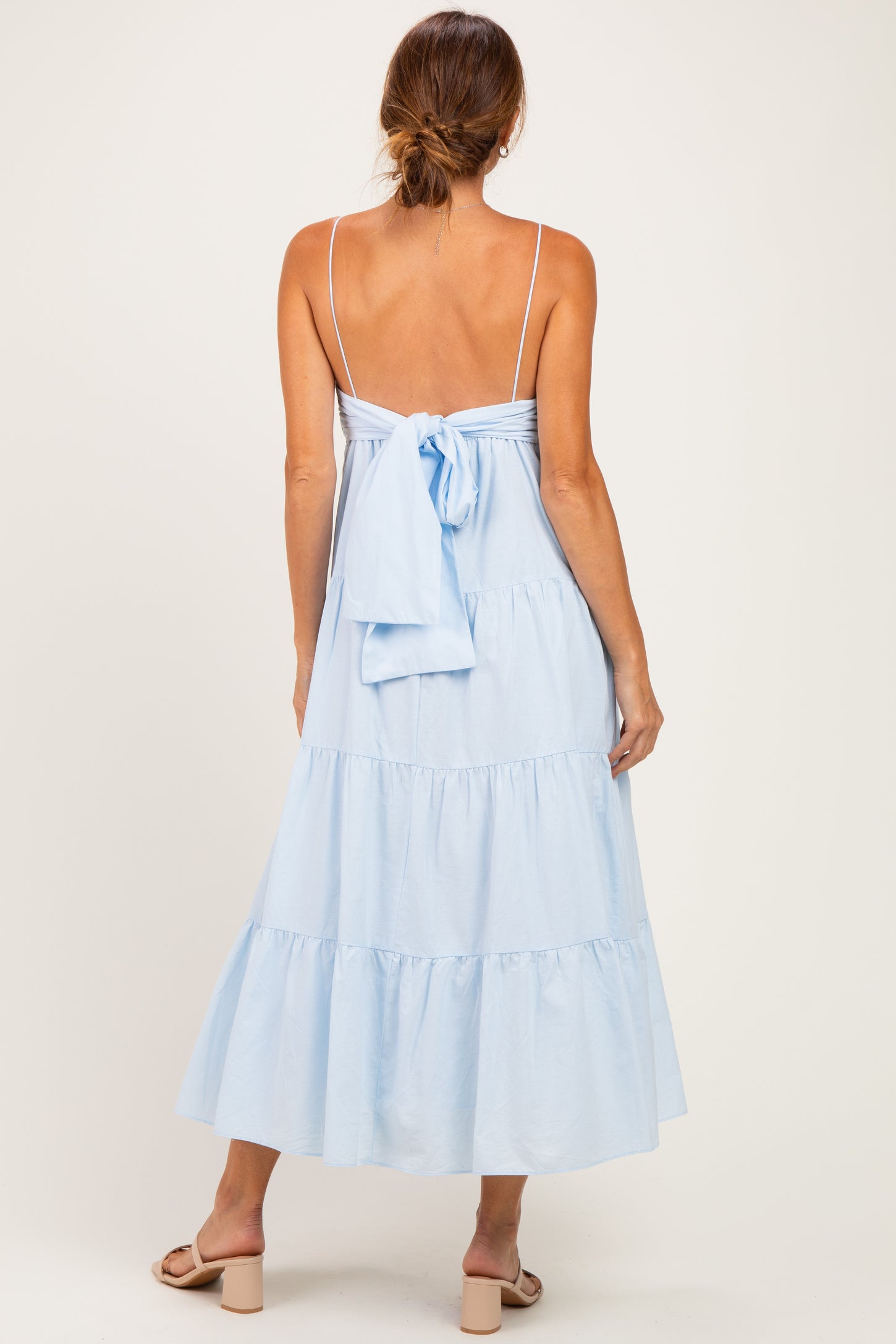 woman wearing a light blue maxi dress with a tiered design and a back tie detail, shown from the back