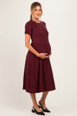 woman wearing a burgundy short sleeve ribbed maternity dress and holding her baby bump