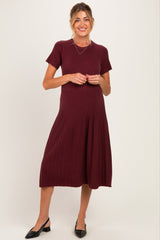 woman wearing a burgundy short sleeve ribbed maternity dress with a flared skirt and a baby bump visible