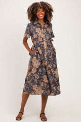 woman wearing a floral maternity dress with short sleeves, a tie waist, and pockets, standing against a plain background