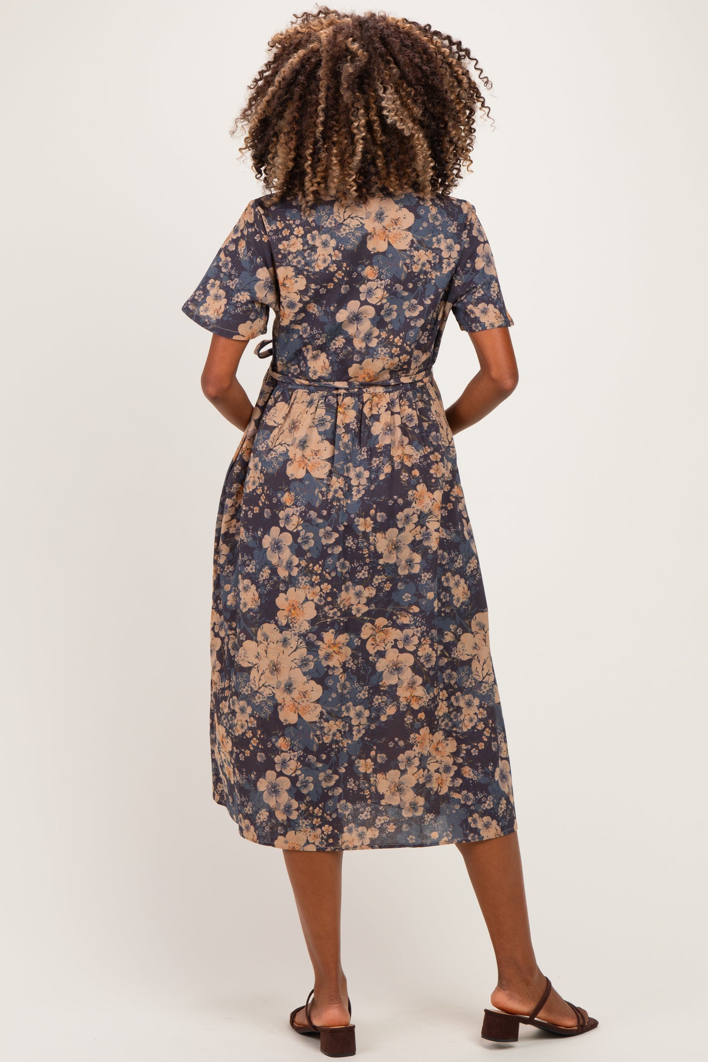 woman wearing a navy blue floral maternity dress with short sleeves and a tie waist detail, showing a baby bump