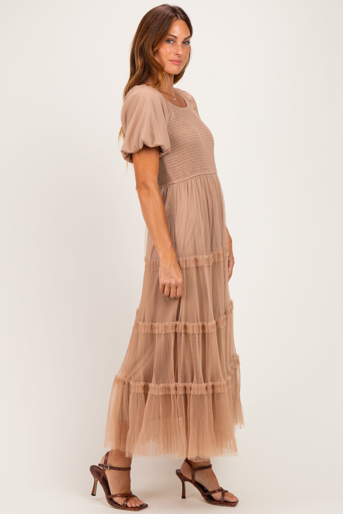 woman wearing a beige puff sleeve maxi dress with tiered tulle skirt and a smocked bodice, standing sideways