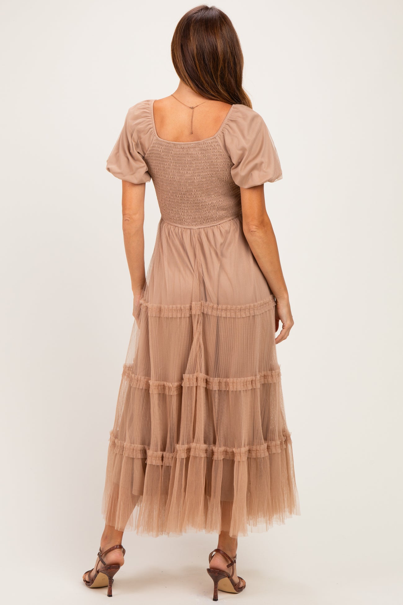 woman wearing a beige maxi dress with puff sleeves and tiered tulle skirt, showing the back view
