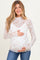 woman wearing a white floral lace long sleeve maternity top and holding her baby bump
