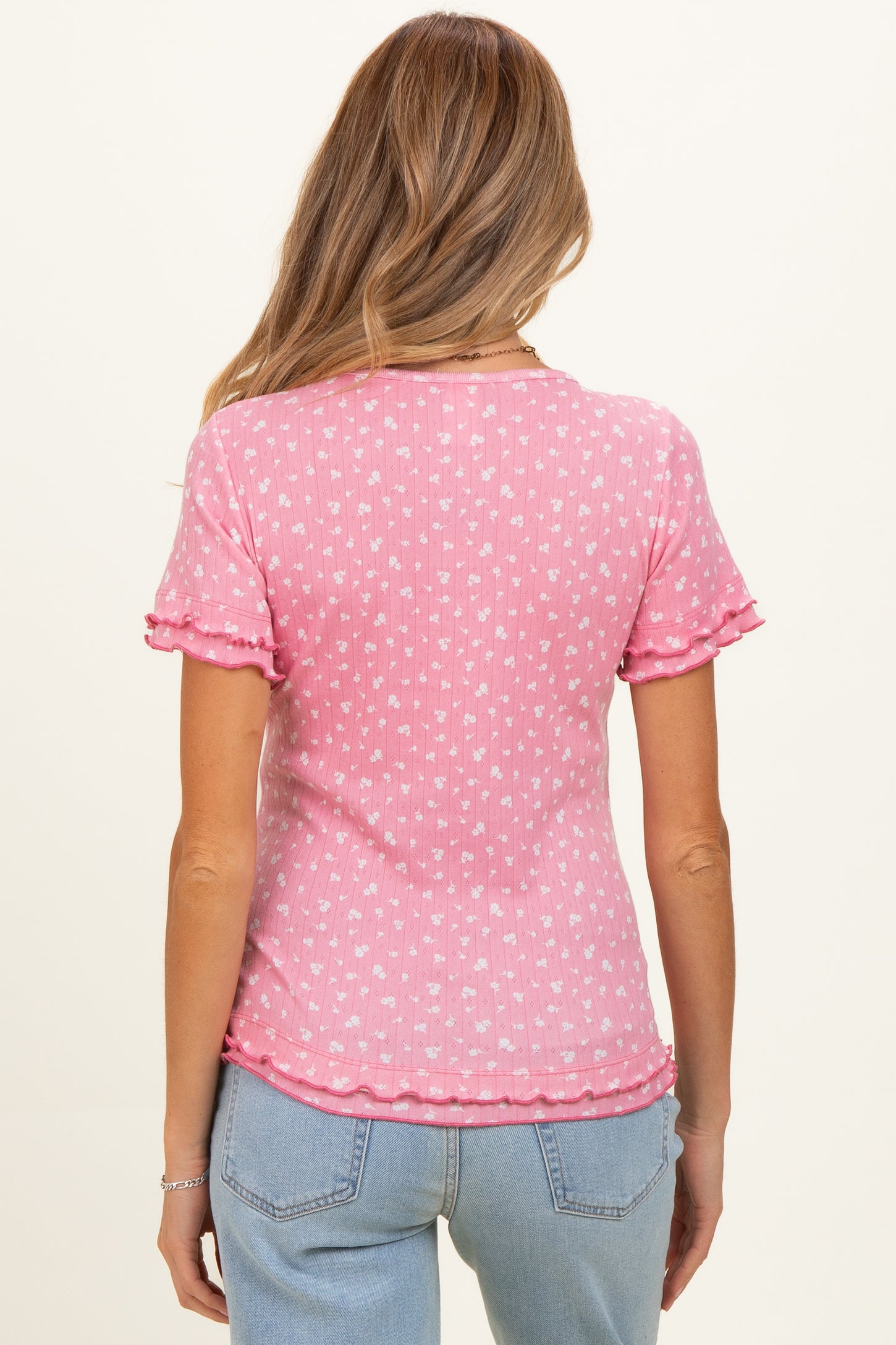woman wearing a pink short sleeve maternity top with a ruffled hem and small white floral prints, seen from the back