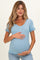 woman wearing a light blue short sleeve maternity top with buttons and ruffled sleeves, holding her baby bump