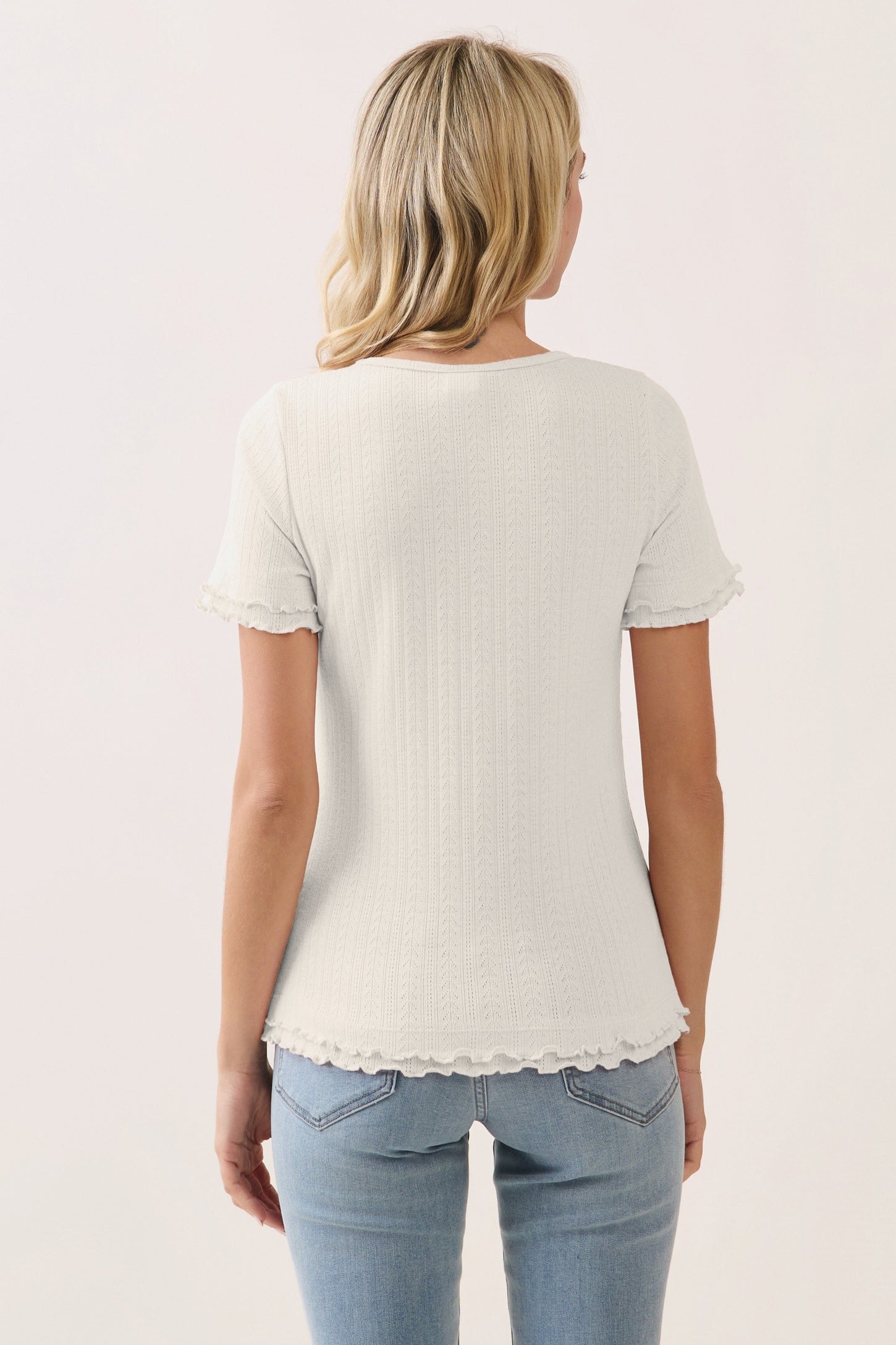 woman wearing a light gray short sleeve top with ruffled edges, paired with blue jeans from the back