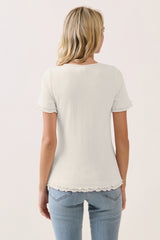 woman wearing a light gray short sleeve top with ruffled edges, paired with blue jeans from the back