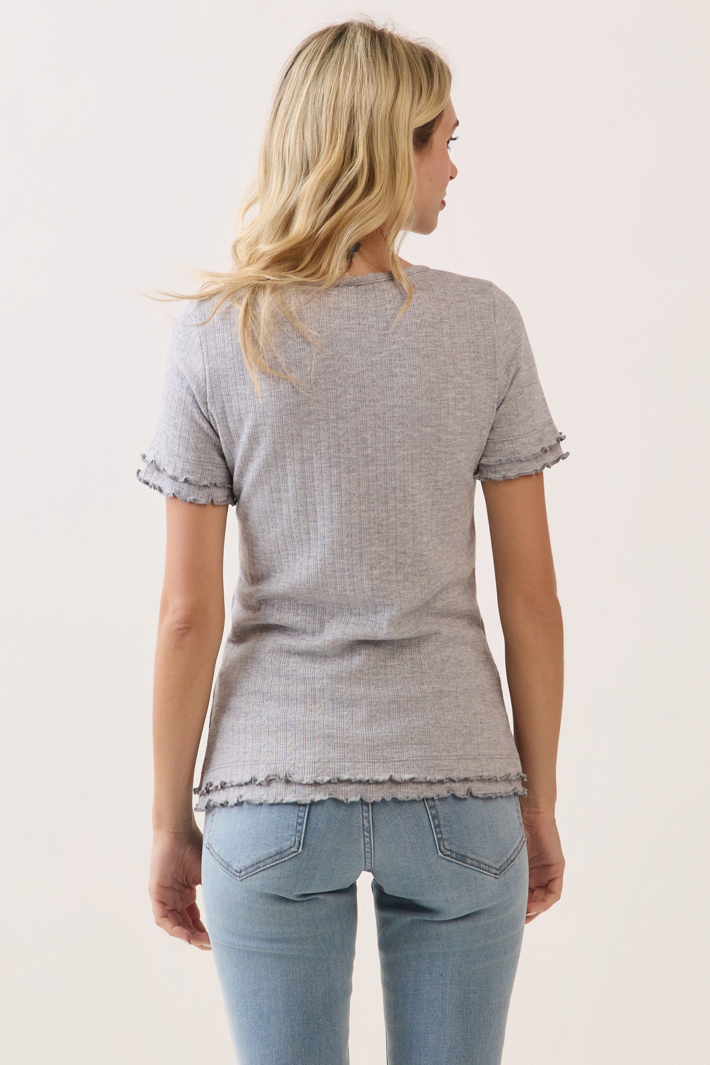 woman wearing a gray ribbed short sleeve top with ruffled edges and light blue jeans, viewed from the back