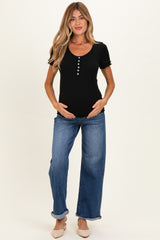 woman wearing a black short sleeve ribbed maternity top and blue wide-leg jeans, holding her baby bump
