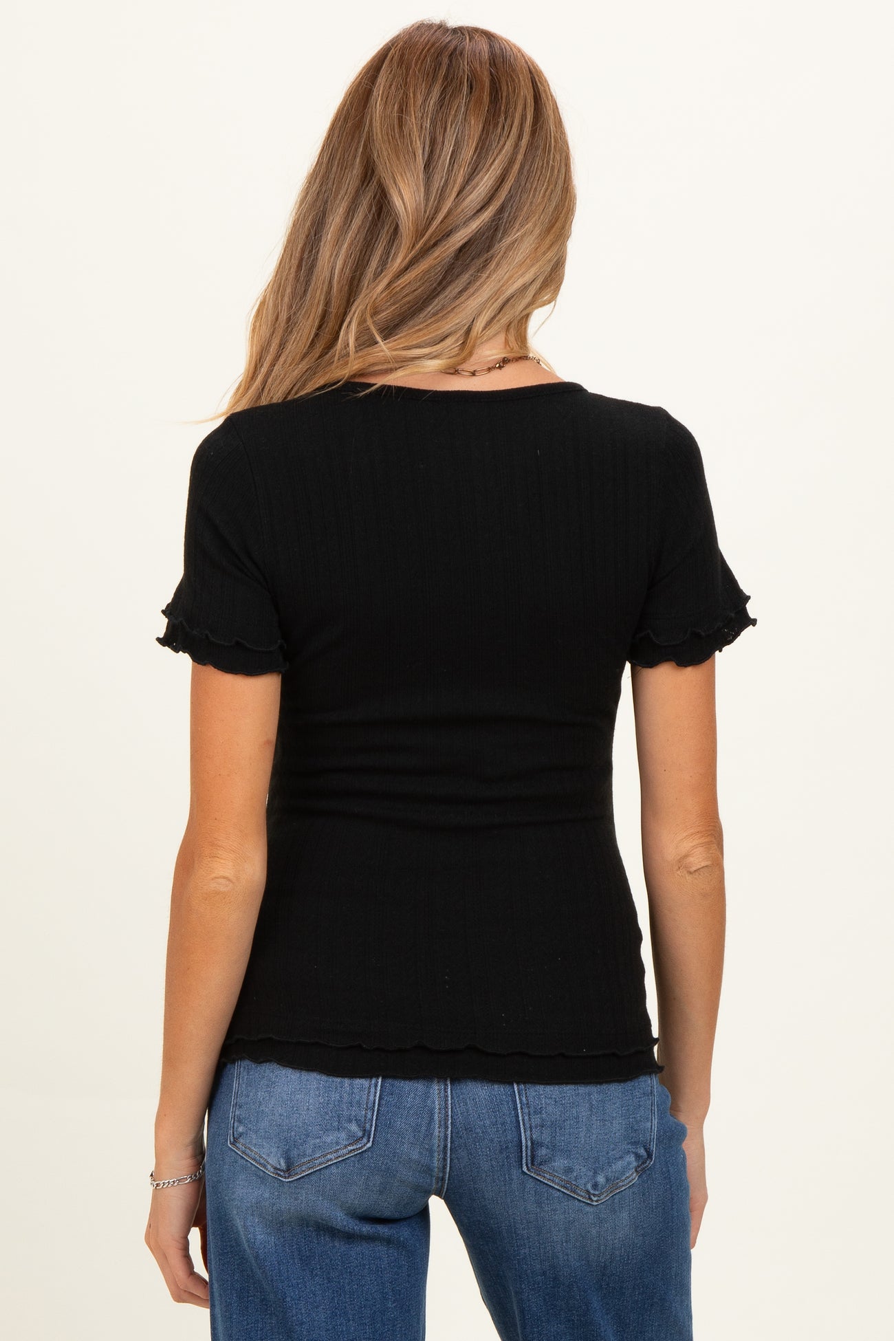 woman wearing a black ribbed maternity top with ruffled short sleeves and a fitted silhouette