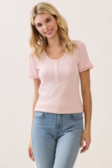 woman wearing a light pink short sleeve knit top with ruffled cuffs and button details, smiling while standing