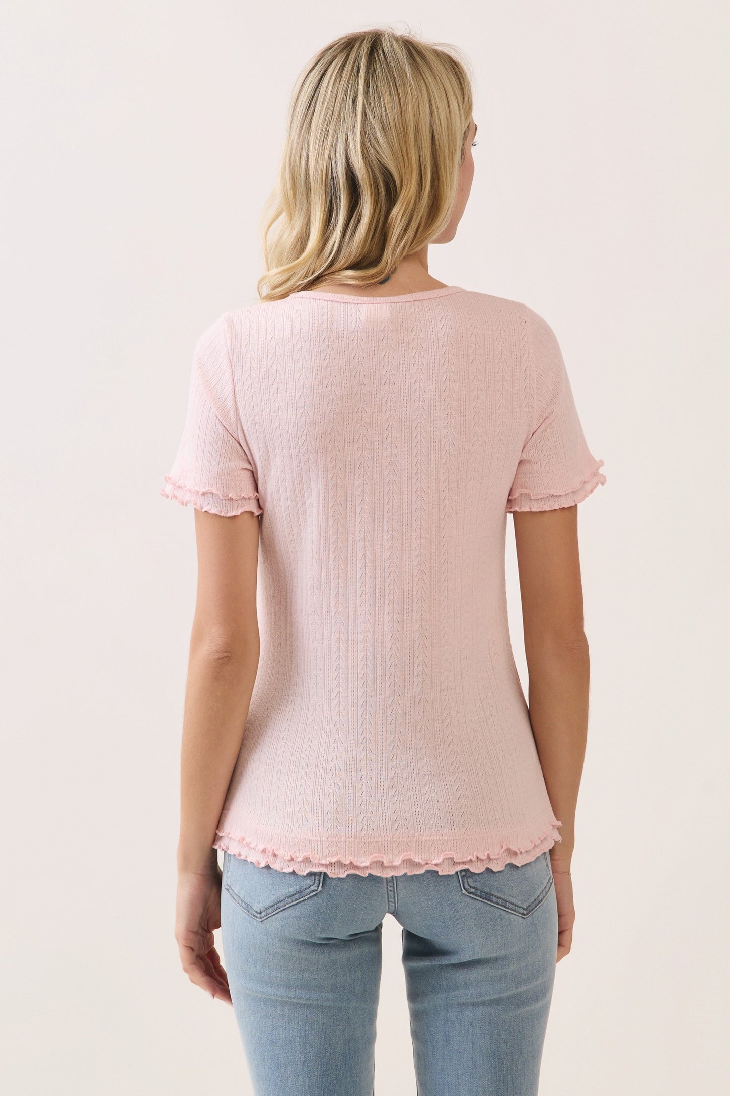 woman wearing a soft pink short sleeve top with ruffled hem and sleeves, styled with light blue jeans