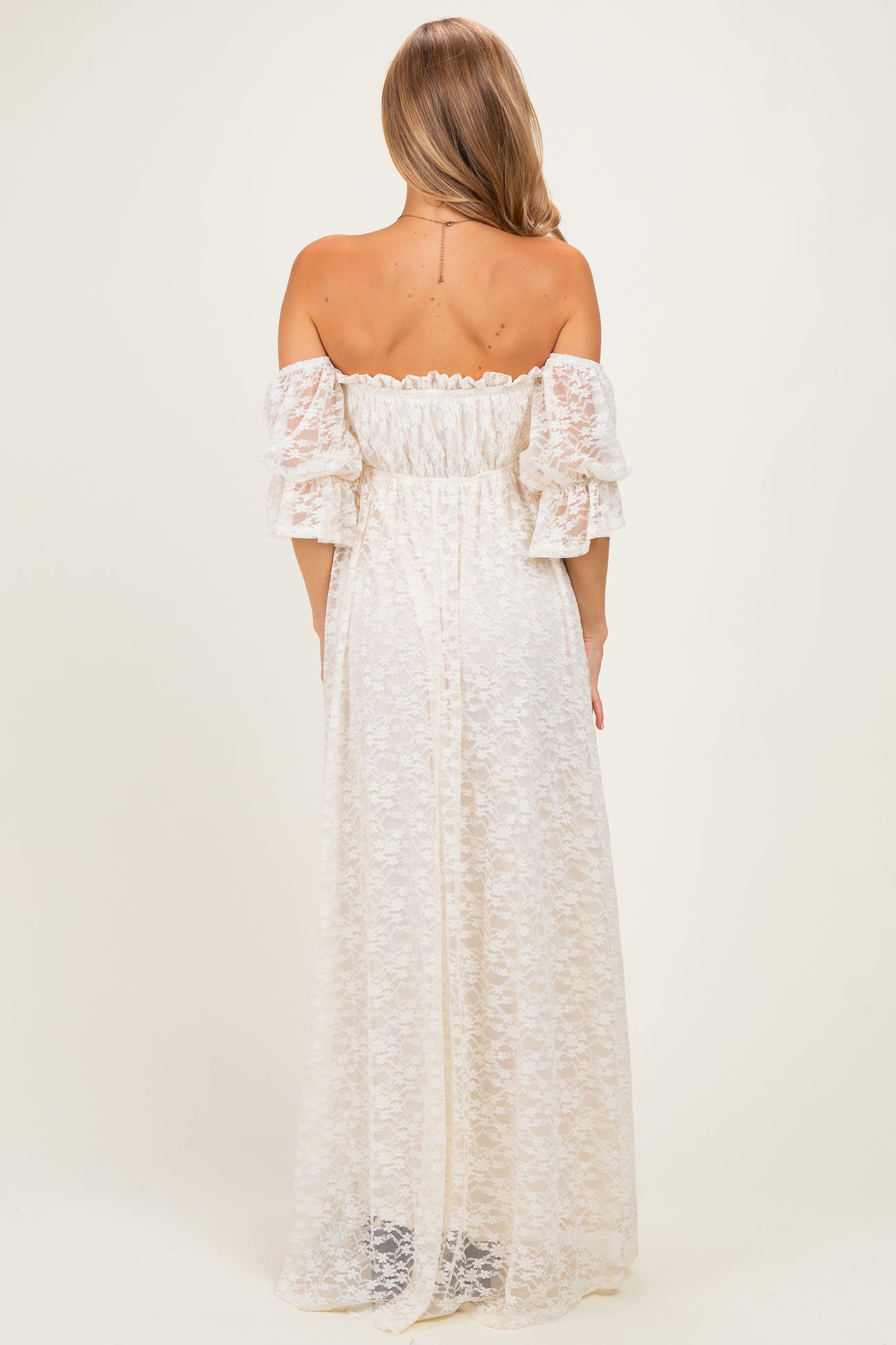 woman wearing a white off-the-shoulder maxi dress with puff sleeves and a floral lace design, viewed from the back