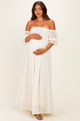woman wearing a white off-the-shoulder lace maternity dress and holding her baby bump
