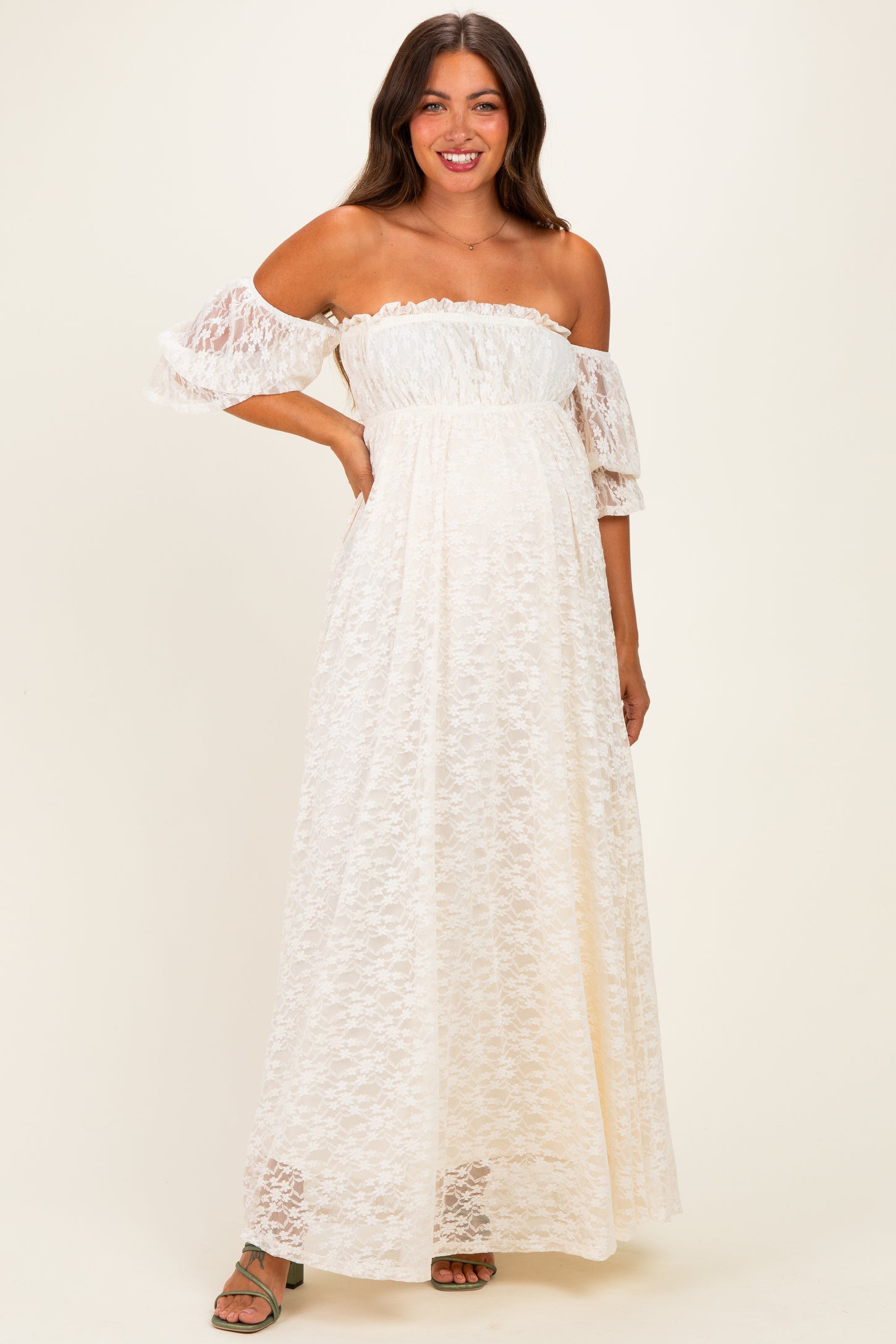 woman wearing a white off-the-shoulder lace maternity maxi dress with puff sleeves and a fitted bodice