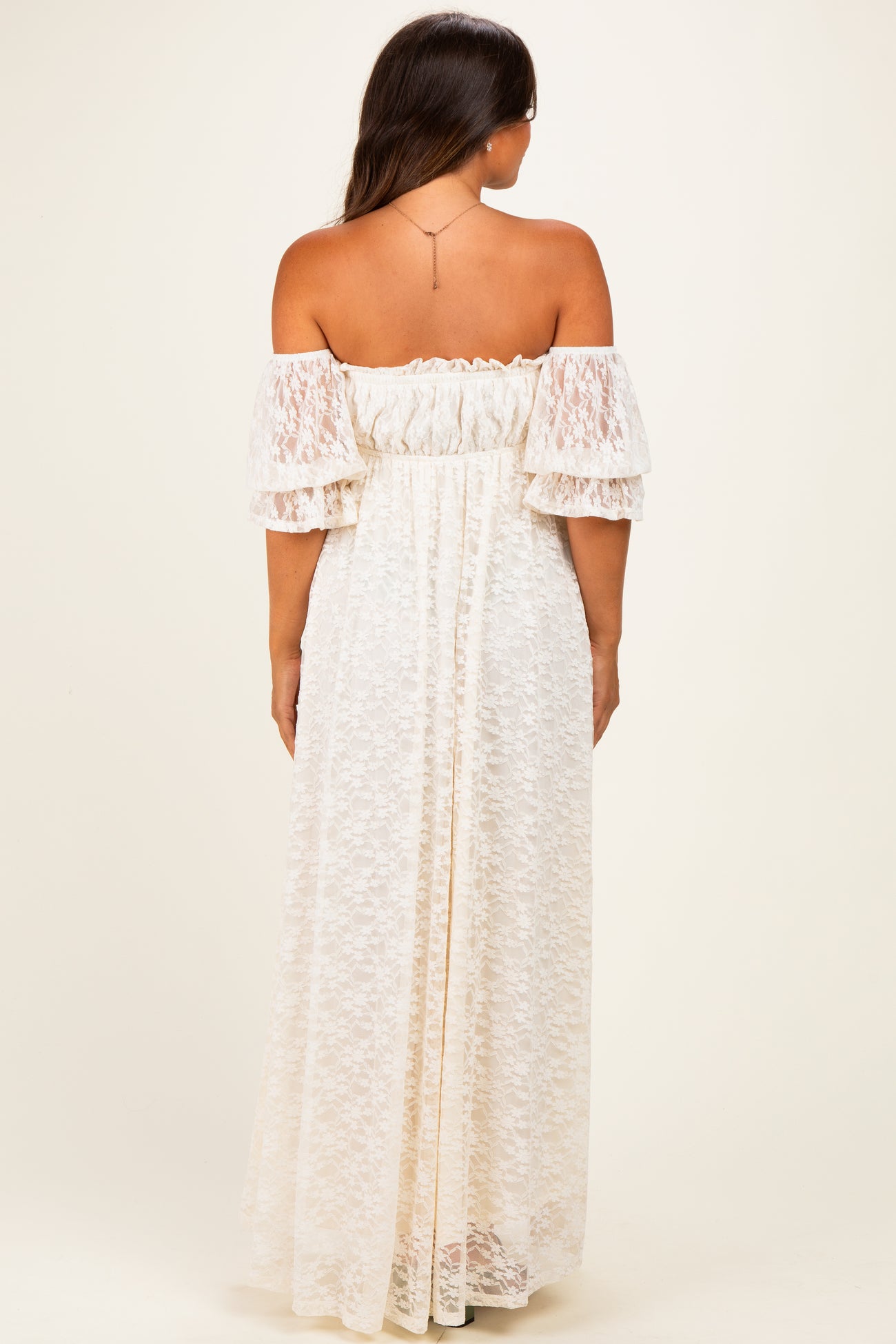 woman wearing a white lace off-the-shoulder maternity maxi dress, showing a relaxed fit and ruffled sleeves from the back