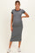 woman wearing a gray maternity dress with black trim and a visible baby bump, standing in white sneakers