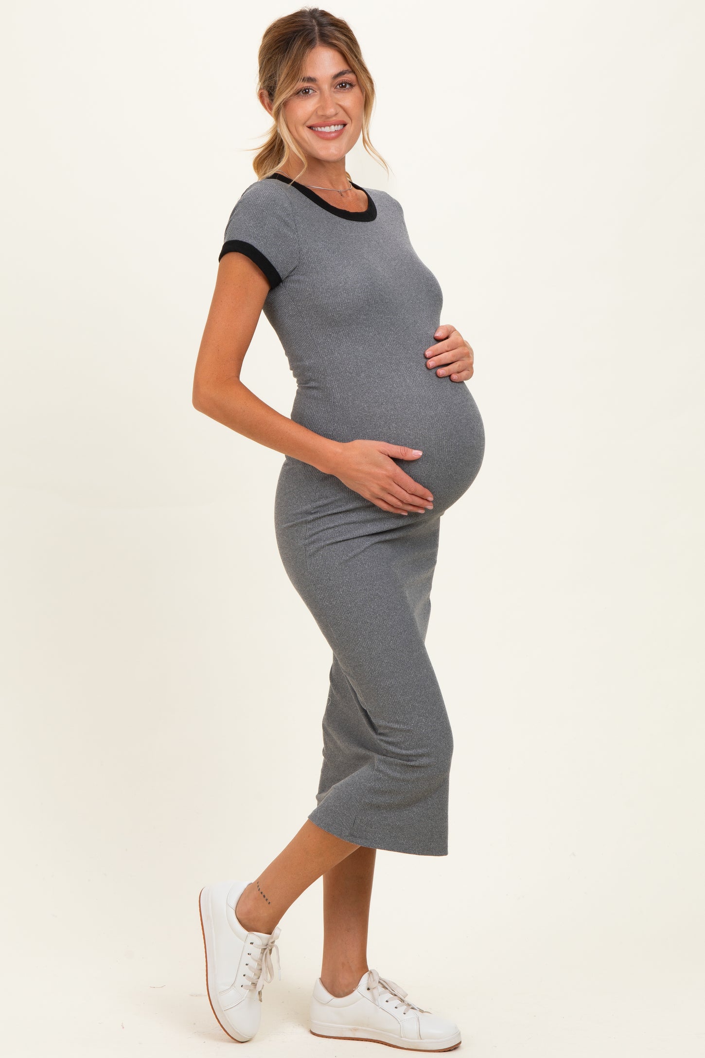 woman wearing a gray maternity dress with black trim and holding her baby bump