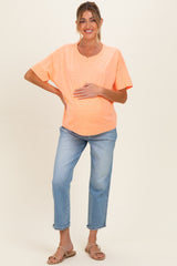 woman wearing a bright orange short sleeve maternity top and blue jeans, holding her baby bump