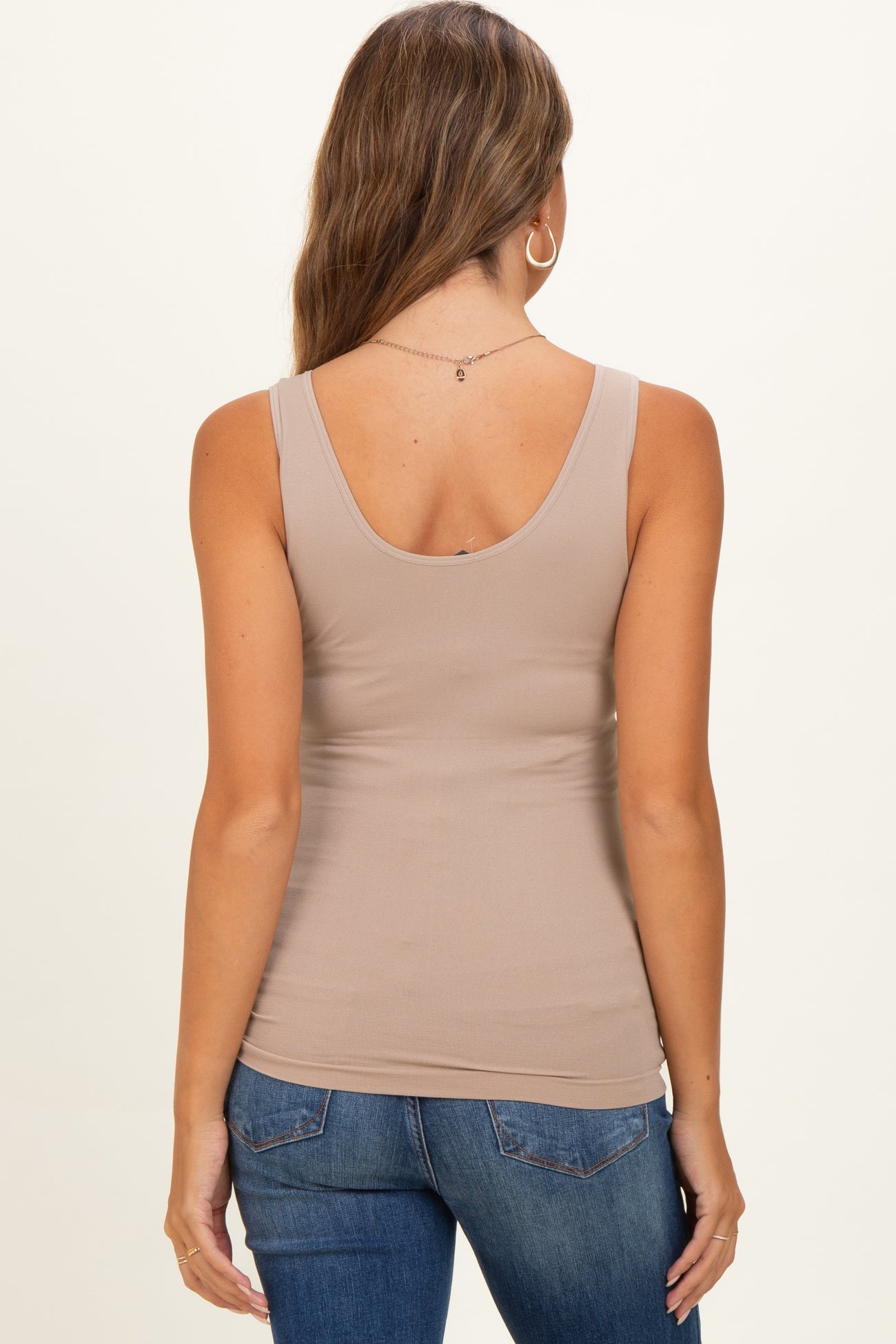 woman wearing a beige maternity tank top from the back, styled with blue jeans