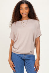 woman wearing a taupe loose-fitting short sleeve top with a round neckline and layered necklaces, paired with denim jeans