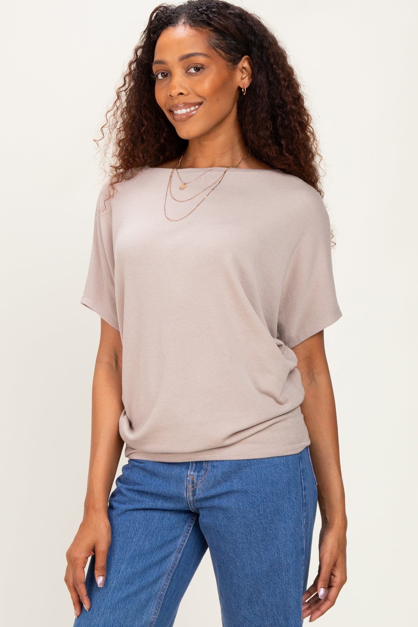 woman wearing a taupe short sleeve top with a relaxed fit paired with blue denim jeans and layered necklaces