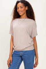 woman wearing a taupe short sleeve top with a relaxed fit paired with blue denim jeans and layered necklaces