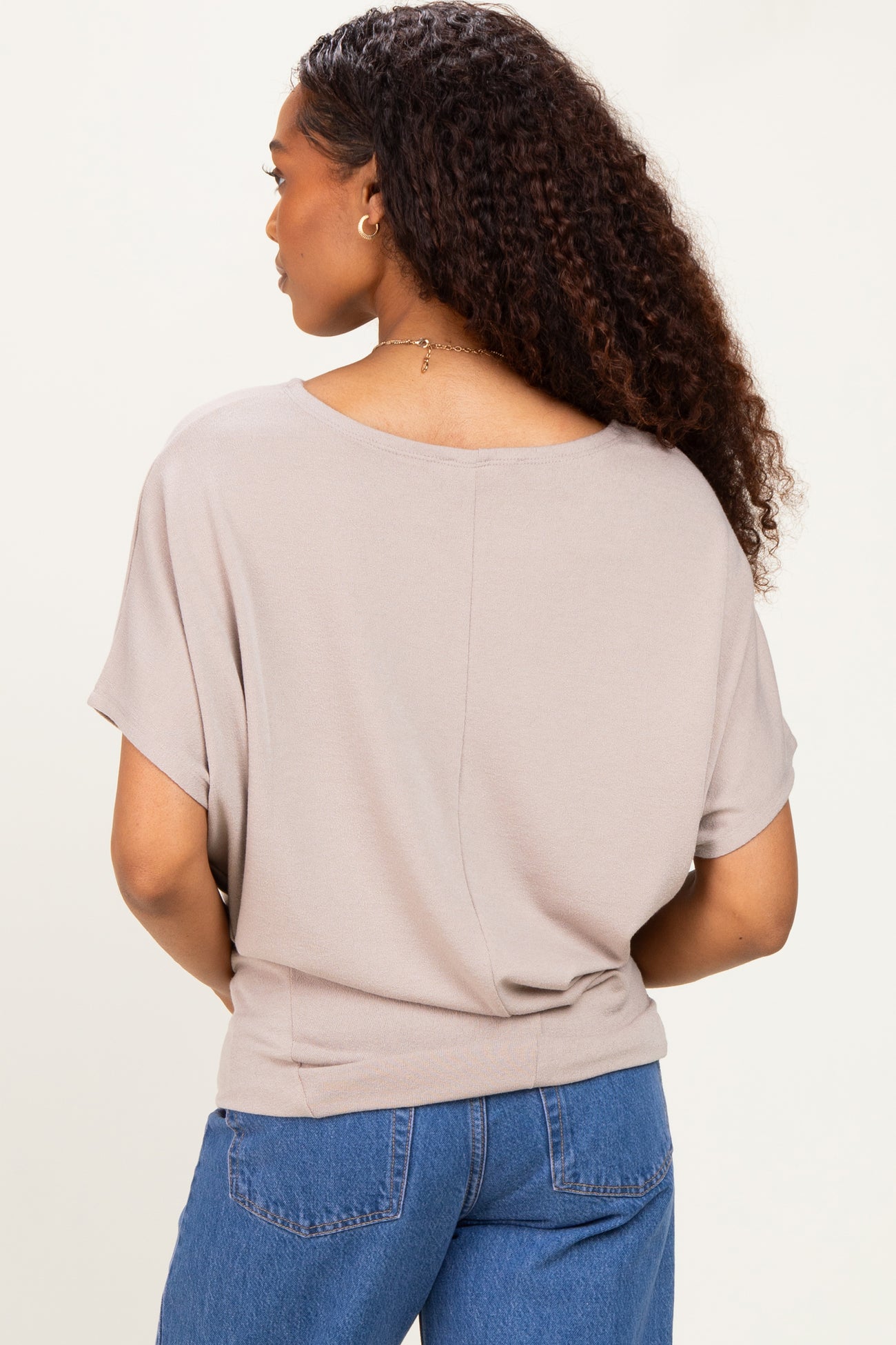 woman wearing a light taupe short sleeve top with a relaxed fit and a round back neckline, seen from behind