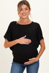 woman wearing a black oversized maternity top and holding her baby bump while smiling